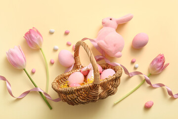 Wicker basket with painted Easter eggs, toy bunny and tulip flowers on yellow basket