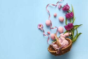 Wicker basket with painted Easter eggs, toy bunny and flowers on blue background