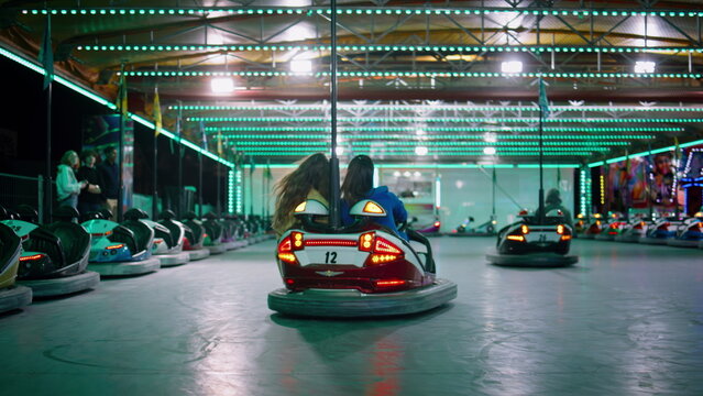 Girls riding bumper car at illuminated amusement park. Excited friends enjoying