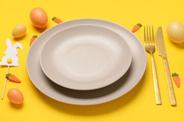 Beautiful Easter table setting served with eggs, toys and bunnies on yellow background