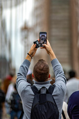 Person with mobile phone photographing the Brooklyn Bridge linking the boroughs of Manhattan and Brooklyn in New York City (USA), the largest suspension bridge in the world until 1889.