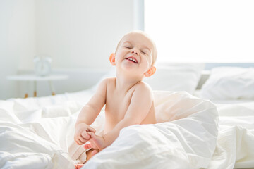 Adorable baby boy in white sunny bedroom.