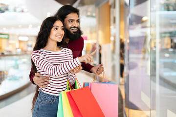 Loving young eastern couple standing in shopping mall with purchases