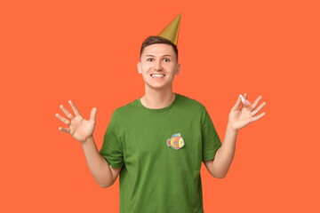 Handsome young man with party whistle and paper fish on orange background. April fool's day...