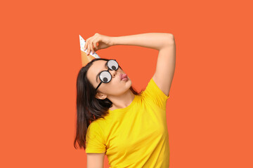 Beautiful young woman in funny disguise on orange background. April fool's day celebration - obrazy, fototapety, plakaty