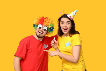 Young surprised friends in funny disguise with paper fishes and whistle on yellow background. April fool's day celebration