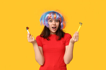Beautiful young shocked woman in funny disguise with party whistles on yellow background. April...