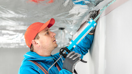 A worker is applies adhesive sealant on the wall for gluing vapor barriers.