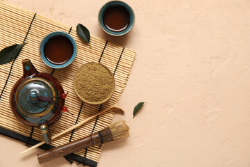 Fototapeta premium Bamboo mat with cups of matcha tea, teapot, chashaku and chasen on beige background