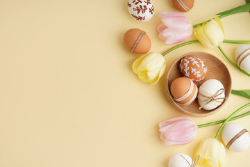 Wooden bowl with Easter eggs and tulips on beige background