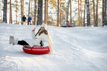 A young girl is tubing in a winter snowy forest with beautiful sunlight