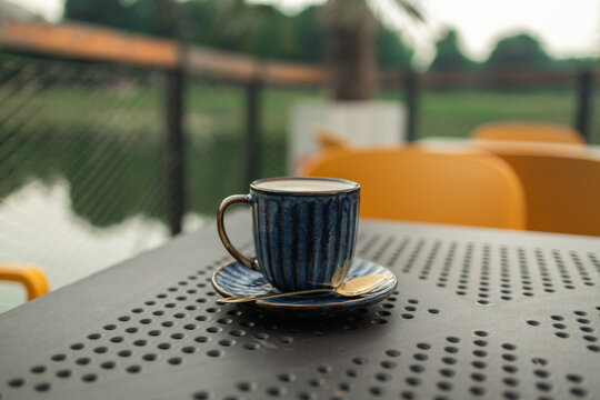 Coffee cappuccino with latte art in blue cup on iron table outdoors in city cafe. Beautiful foam, greenery ceramic cup. Morning in a luxury hotel. High quality photo