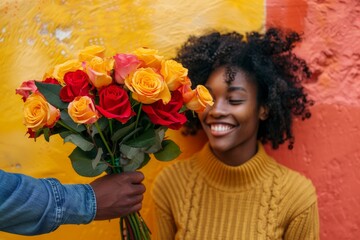 A joyous woman stands against a wall, adorned with a vibrant bouquet of yellow and orange roses, her beaming smile a perfect reflection of the floral design she holds in her hands