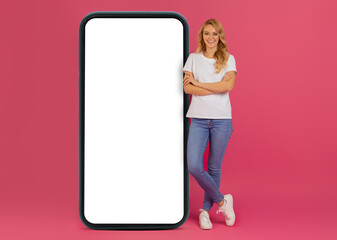 Cheerful Blonde Young Woman Standing Near Big Smartphone, Pink Background