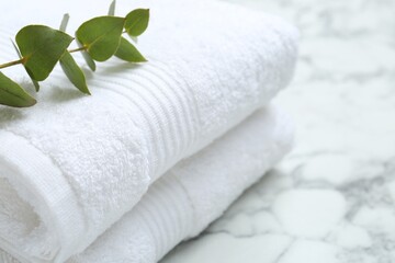 Fototapeta na wymiar Folded terry towels and eucalyptus branch on white marble table, closeup