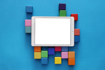 Modern tablet and cubes on light blue background, flat lay. Space for text