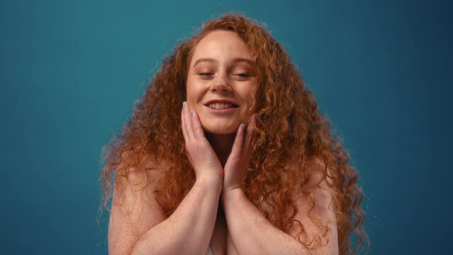 Young pretty redhead plus size or plump woman celebrating her natural body. Positive beautiful female model in white underwear against blue background. Lifestyle portrait with minimal makeup