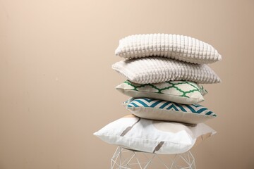 Stack of soft pillows on small table near beige wall. Space for text
