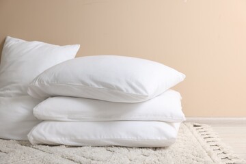 Fototapeta na wymiar Soft white pillows near beige wall indoors. Space for text