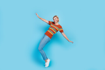 Fototapeta na wymiar Full size photo of funny positive gorgeous woman dressed knit t-shirt denim pants dancing on tiptoes isolated on blue color background