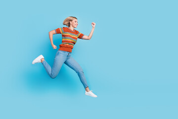 Fototapeta na wymiar Full size photo of fast active woman dressed knit t-shirt clenching fists run shopping to empty space isolated on blue color background