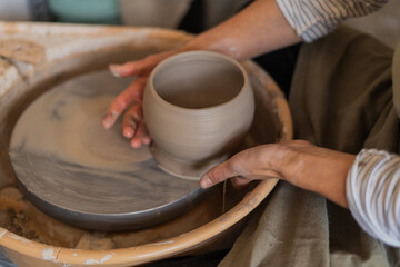 A potter carefully separates a newly shaped clay pot from the spinning wheel, illustrating the...