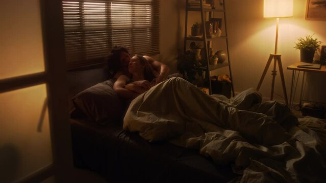 Young affectionate couple in love lying together in bed under blanket and enjoying romantic night at home