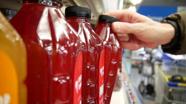 Close-up of many berry juice bottles standing in a row in a supermarket and a male buyer's hand taking one