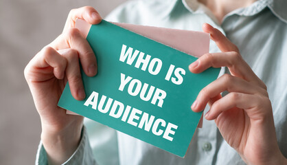 Who is Your Audience text on blank business card being held by a woman's hand with blurred...