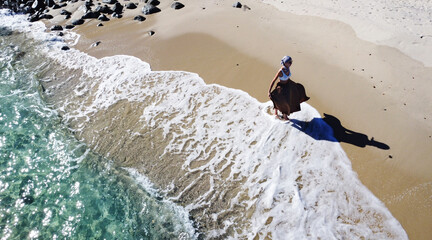 Aerial view of woman walking on the sandy beach with ocean waves braking on the coast