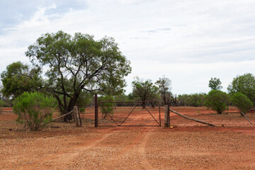 Fototapeta premium A rural scene in the outback with a gate and fence in typical red-coloured dirt