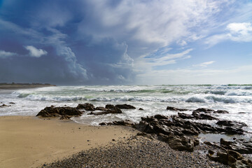 Fototapeta na wymiar Baie d'Audierne en Bretagne : sable, rochers, océan agité aux reflets émeraude sous un ciel aux nuages contrastés.