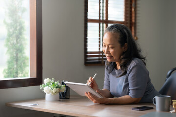 Confident mature asian businesswoman working with a tablet in her well-organized home office.
