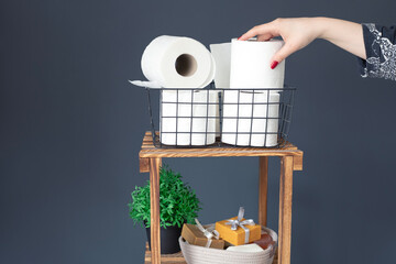 Woman taking toilet paper from wooden shelving unit.