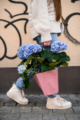 Woman florist carrying bouquet of fresh hydrangea flowers in blue colors wrapped in pink paper bag