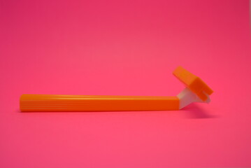 Things, personal care products, disposable, plastic, orange razor, located on pink background.