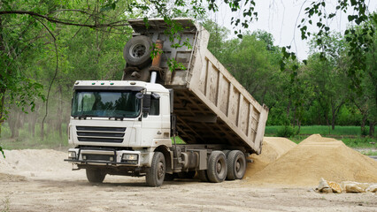 Fototapeta na wymiar A heavy service truck - dump truck unloads sand among trees, in a forest or park. Environmental problems. Photo