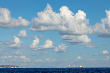 cargo ship nearby Capo Peloro Lighthouse in Punta del Faro on the Strait of Messina, most north...