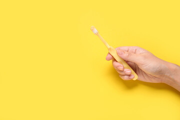 Female hand with toothbrush on yellow background.