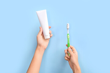 Female hands with toothbrush and toothpaste on blue background.