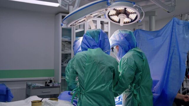 Surgeons in robes and helmets operating a patient under round lamps. Process of trauma surgery in modern clinics.