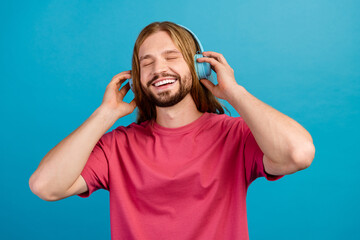 Portrait of cheerful peaceful young man closed eyes hands touch headphones isolated on blue color background