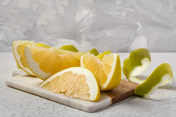 Board with tasty pomelo slices and peel on white table