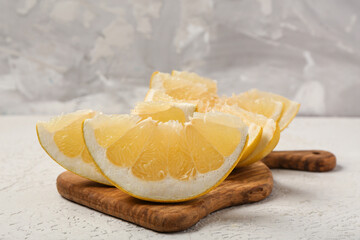 Wooden board with ripe pomelo slices on white table