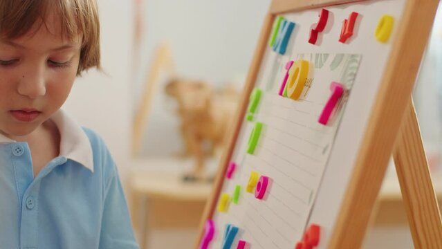 Focused child learning numbers with magnetic board. Early education and cognitive development concept. Design for educational resources, learning aids. Close-up shot with selective focus and place for