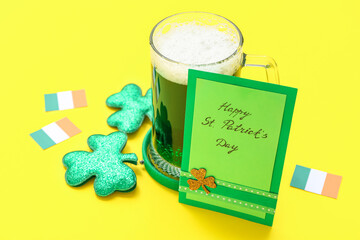 Glass of beer with greeting card, headband and Irish flags on yellow background. St. Patrick's Day...