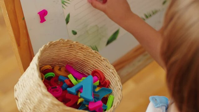 Child selecting magnetic letters from a basket. Literacy development and alphabet recognition concept. Design for educational resources, language learning. Close-up shot with selective focus and place