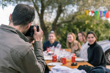 Young man taking a picture of girls sitting at the table during a birthday party with a reflex camera