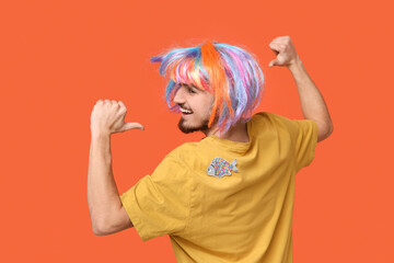 Handsome young man in funny disguise with paper fish attached to his back on orange background. April fool's day celebration