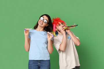Young friends in funny disguise with party whistles on green background. April fool's day...